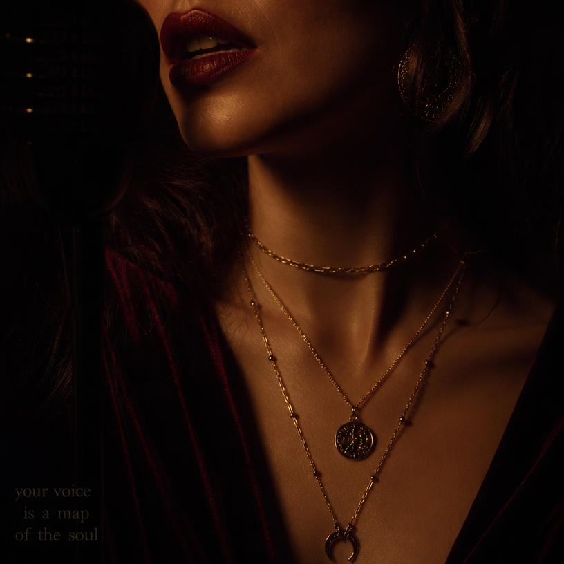 Close portrait of a woman speaking, wearing layered gold necklaces